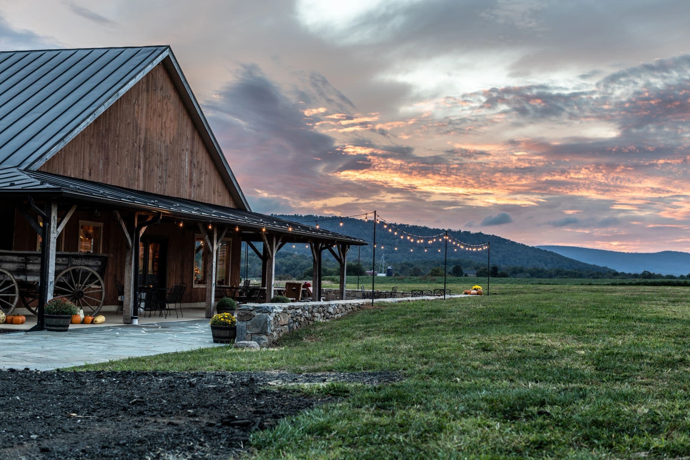 The timber-frame porch at sunset, string lights over the lawn, and the Hillsboro Gap beyond the fields.